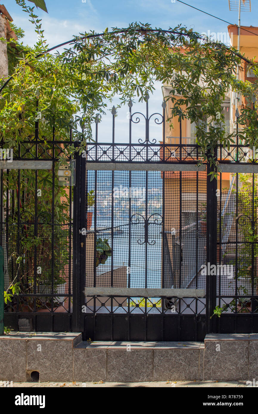 The architecture of Kavala - a beautiful iron gate with climbing plants, through which the harbor is seen. Stock Photo