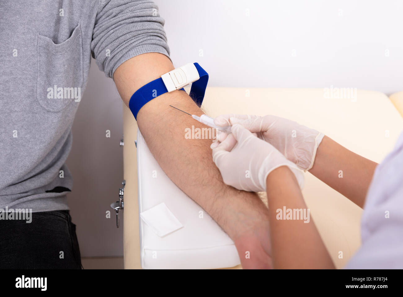 Young Female Doctor Injecting Male Patient With Syringe To Collect Blood Sample In Clinic Stock Photo