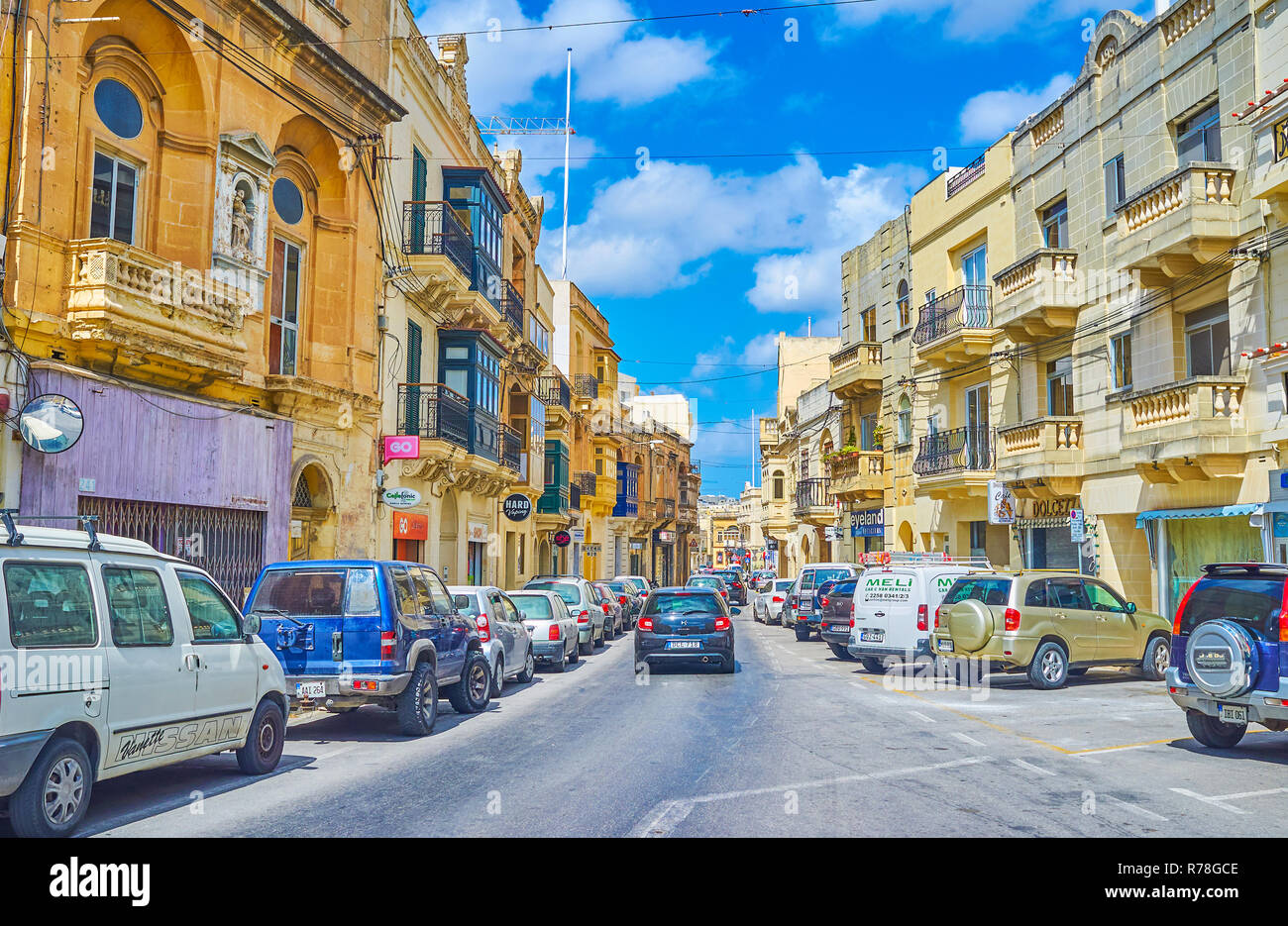 MOSTA, MALTA - JUNE 14, 2018: The busy traffic in Il-Kbira street, lined with old mansions, stores and cafes, on June 14 in Mosta. Stock Photo