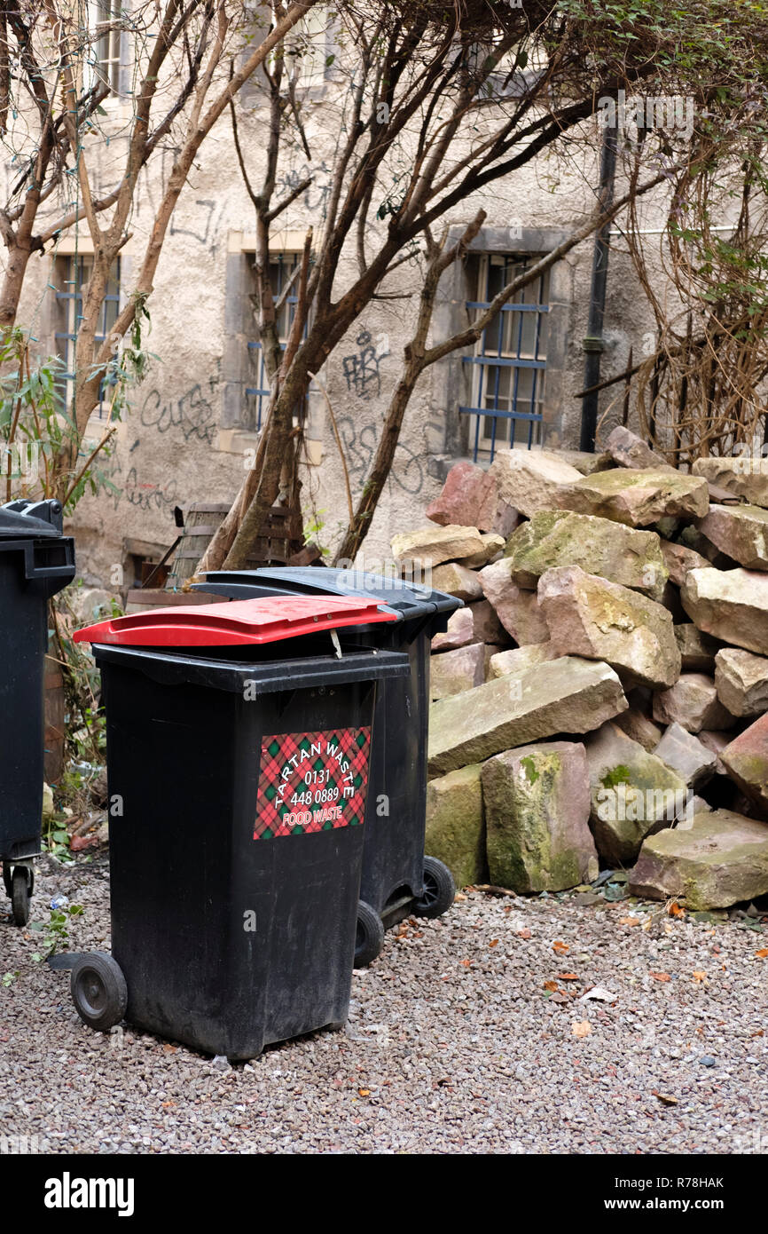 A black food waste wheelie bin, behind old buildings in the Cowgate