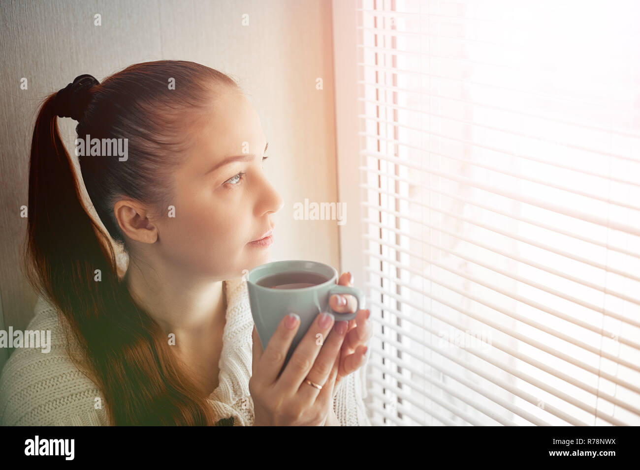 drinking tea sitting on the window of Caucasian beautiful middle-aged woman with red hair, toning Stock Photo