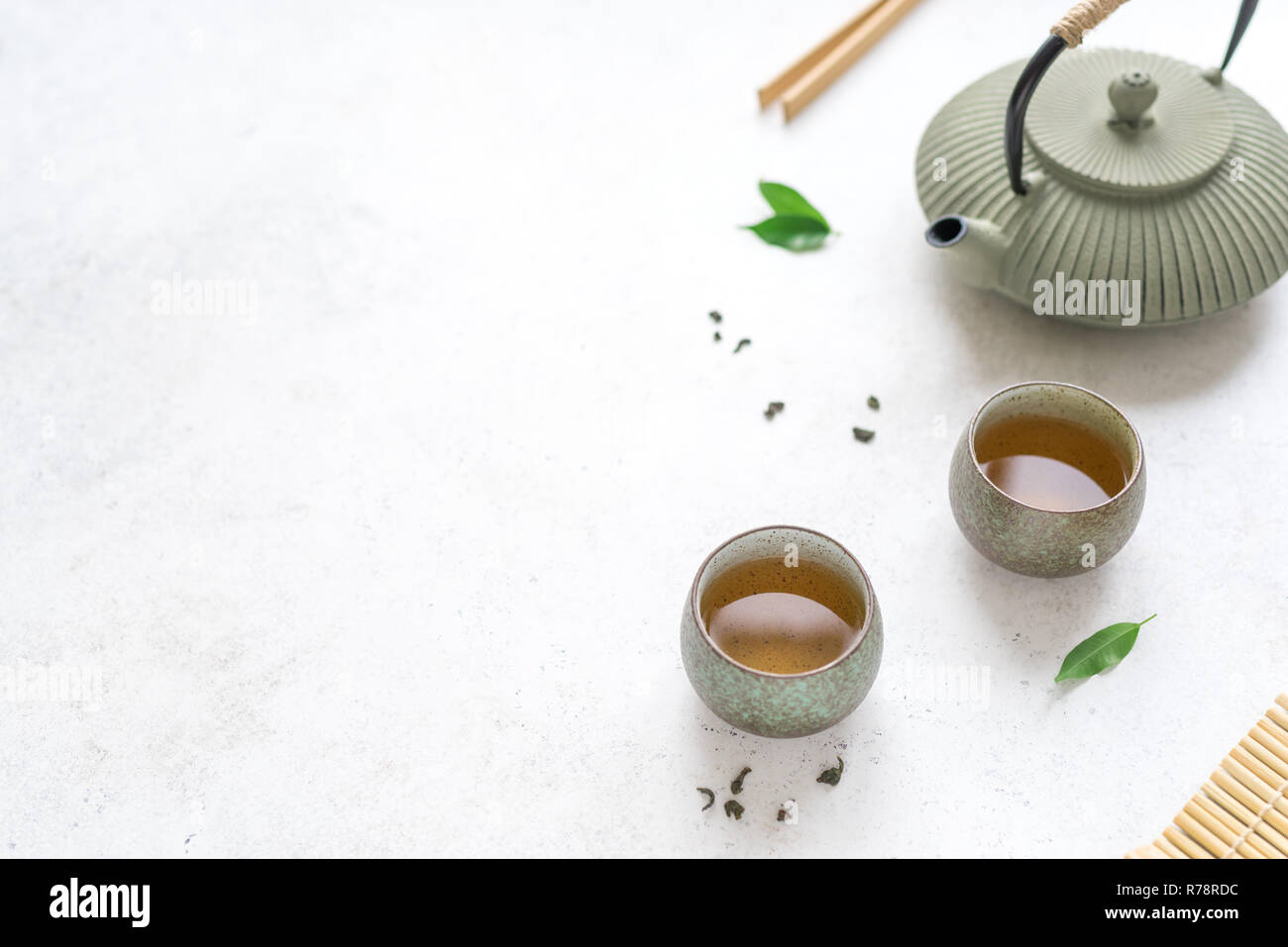 Chinese Tea Set -  iron teapot and ceramic teacups with green tea and leaves. Traditional tea composition on white background, copy space. Stock Photo