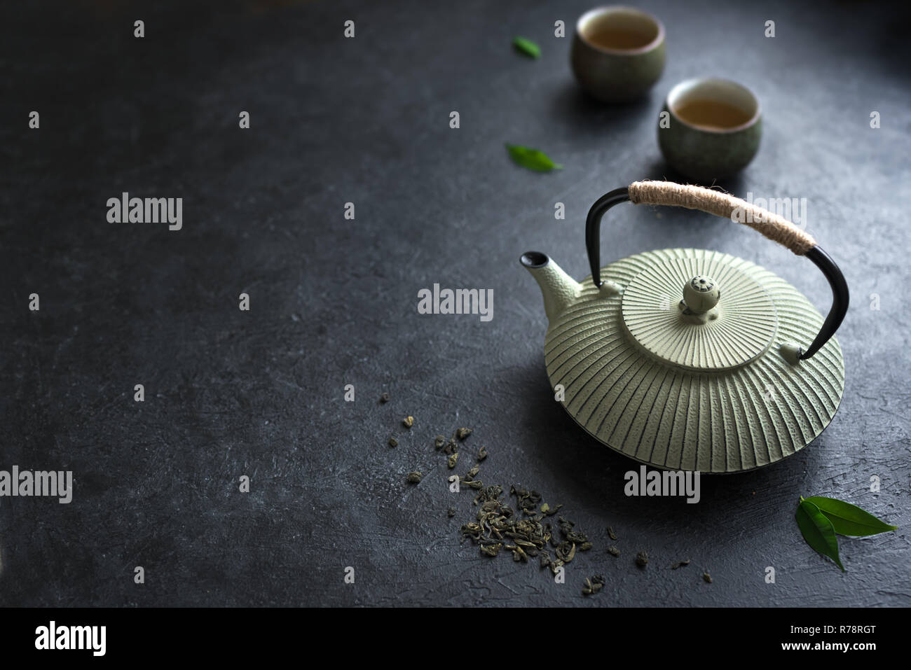 https://c8.alamy.com/comp/R78RGT/teapot-and-teacups-on-black-background-copy-space-traditional-asian-tea-set-iron-teapot-and-ceramic-teacups-with-green-tea-and-tea-leaves-R78RGT.jpg