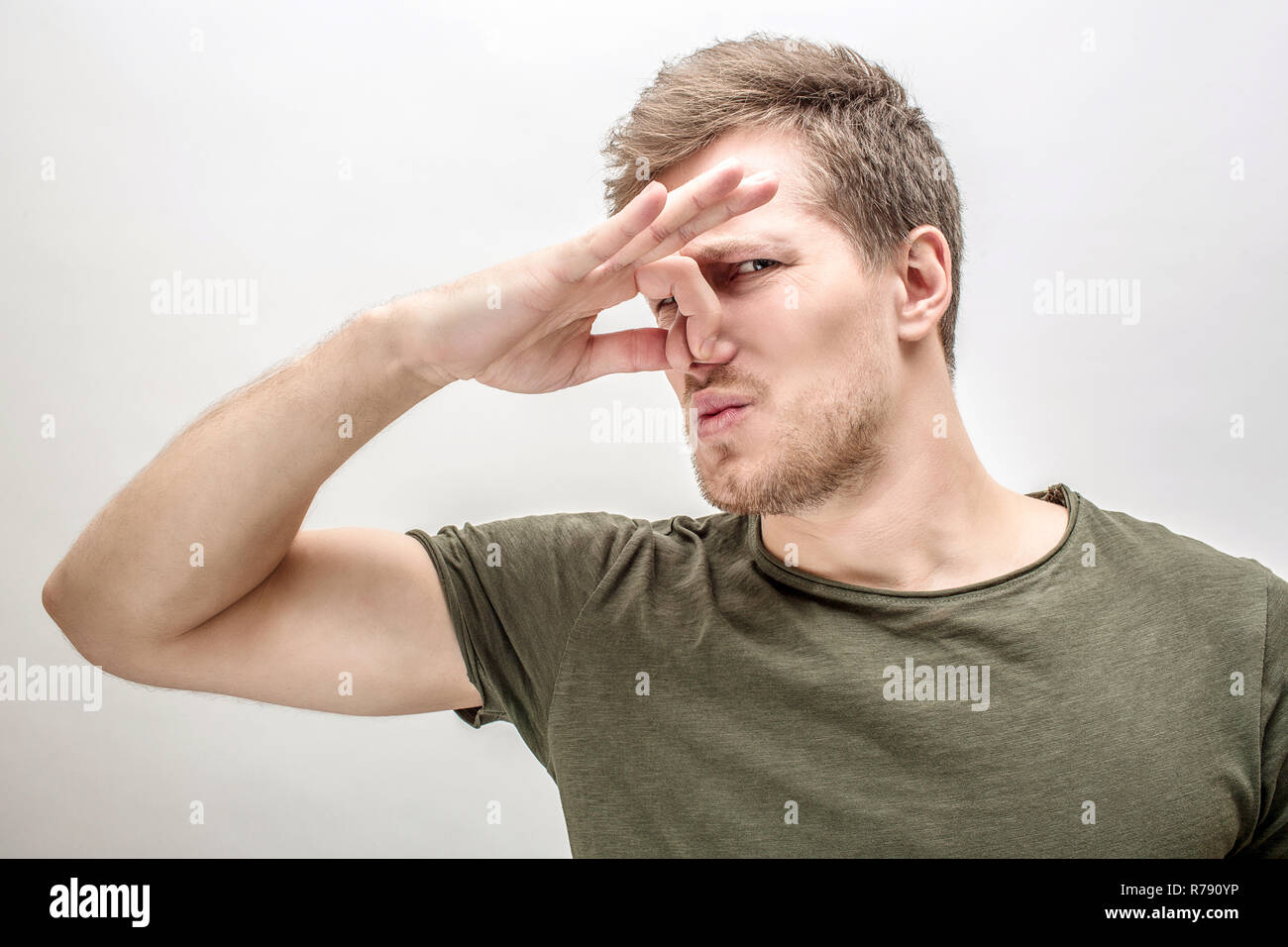 Young man keeps nose closed. He smells bad smell. Isolated on white
