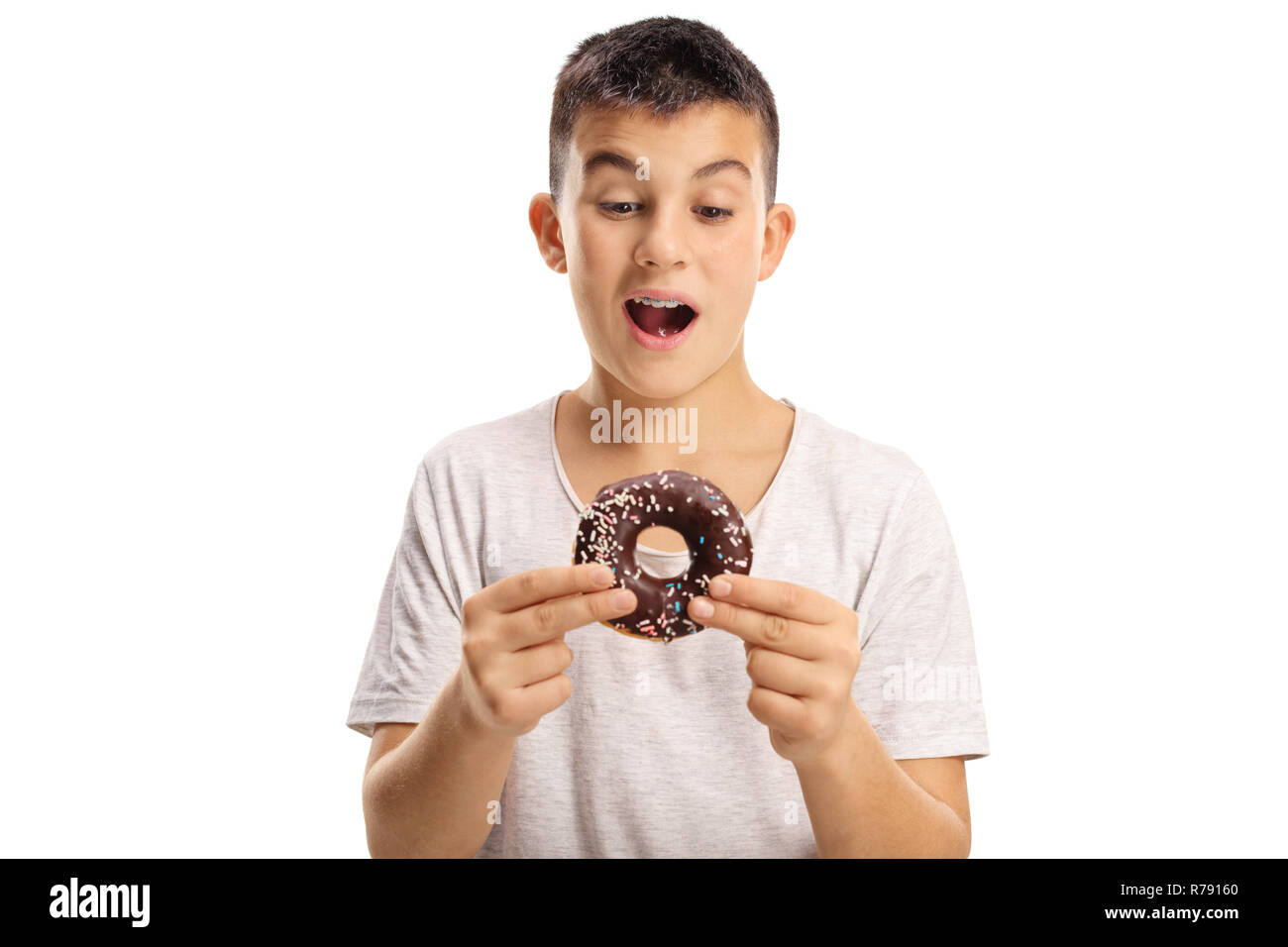 Teenage boy holding a chocolate donut about to bite it isolated on white background Stock Photo