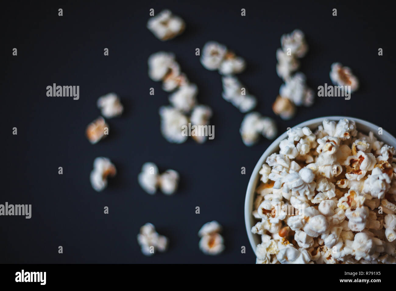 Top view of popcorn in a ceramic bowl on a matte black surface. Tasty