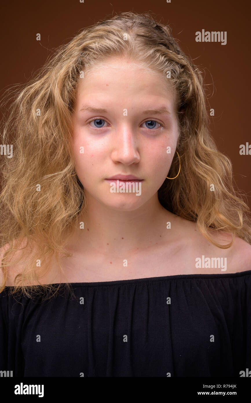 Face of young beautiful blonde teenage girl against brown background Stock Photo