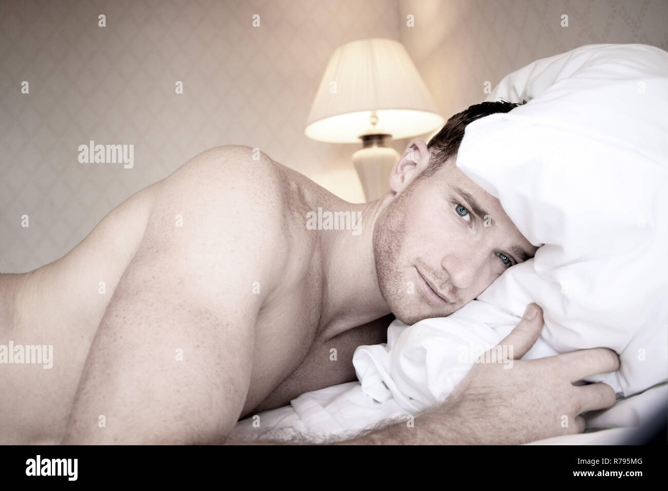 Good looking nude muscular man with blue eyes lying on hotel bed sheets  looking at camera Stock Photo - Alamy