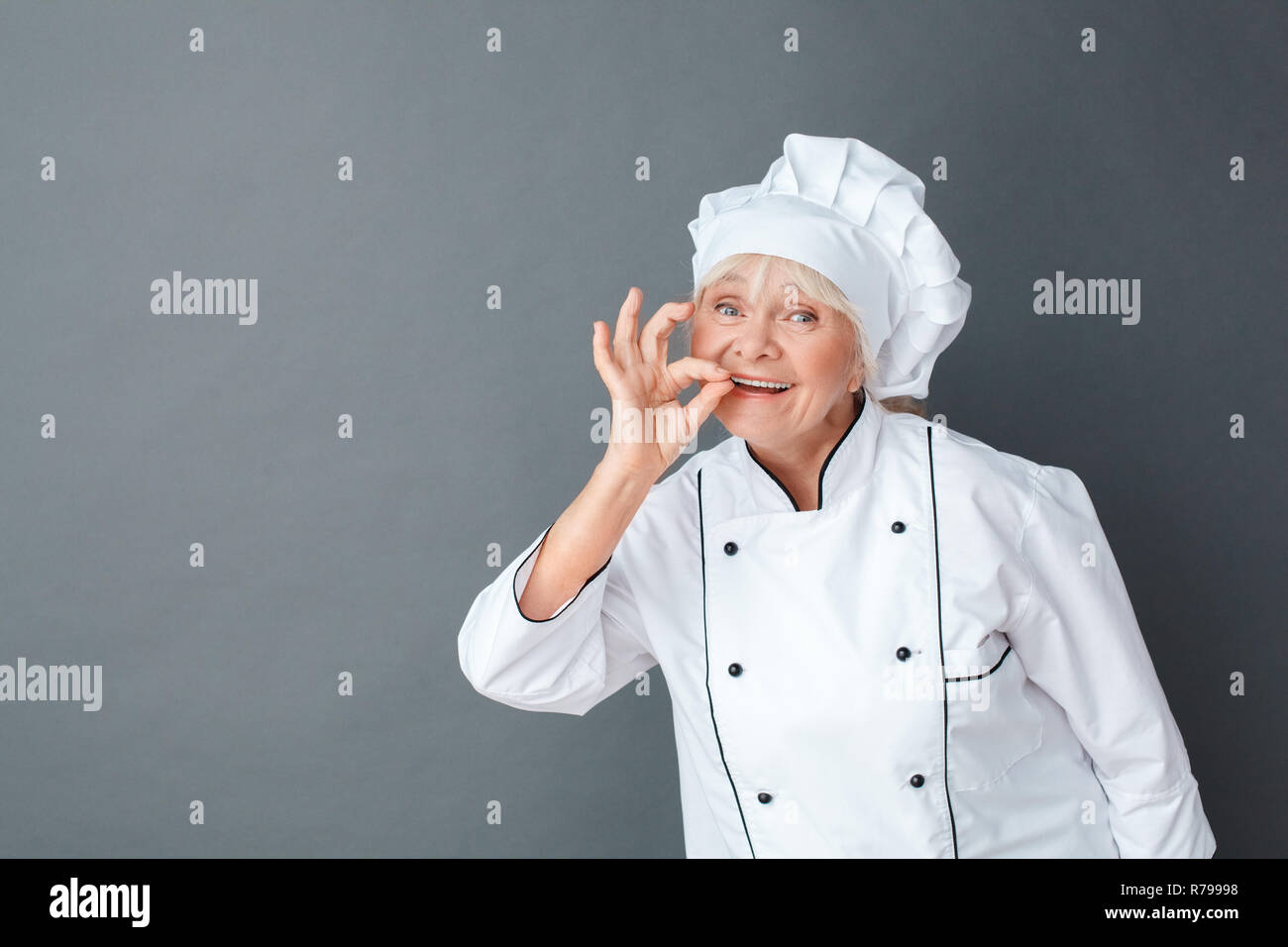 Senior woman chef studio standing isolated on gray showing ok sign ...