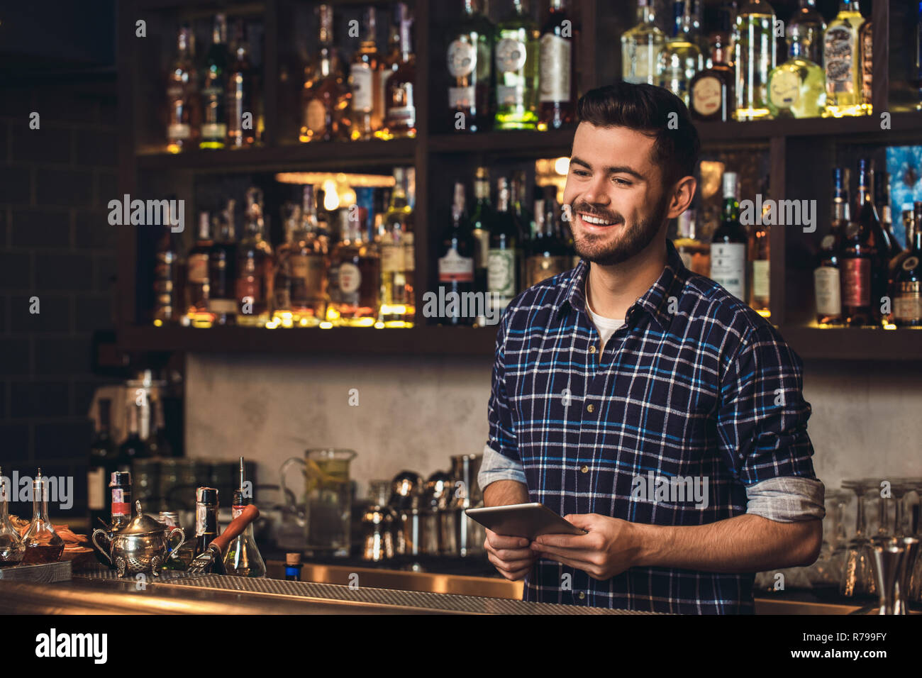 Young bartender standing at bar counter holding digital tablet laughing joyful Stock Photo