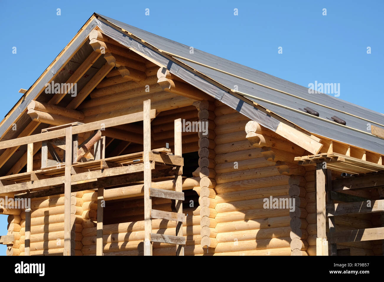 Process of wooden rural house straight roof slope mounting on cloudless sunny day front view. Wooden country house construction Stock Photo