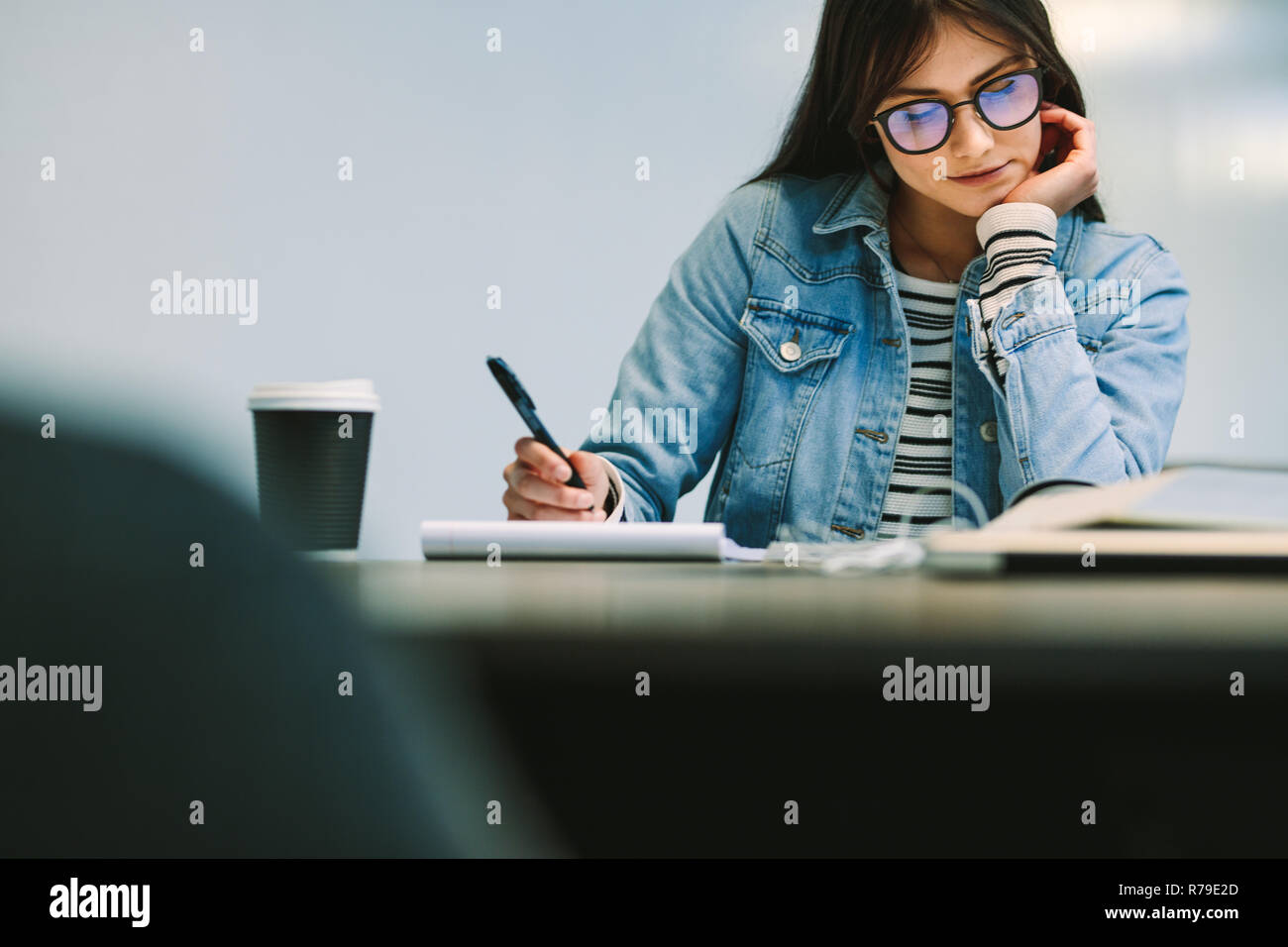 Happy female student sitting at college library and making notes. Woman studying at university library. Stock Photo