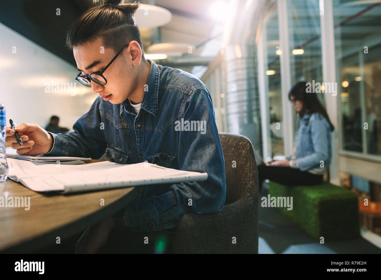 Young male student studying at college library. Man reading book and making notes at university campus. Stock Photo