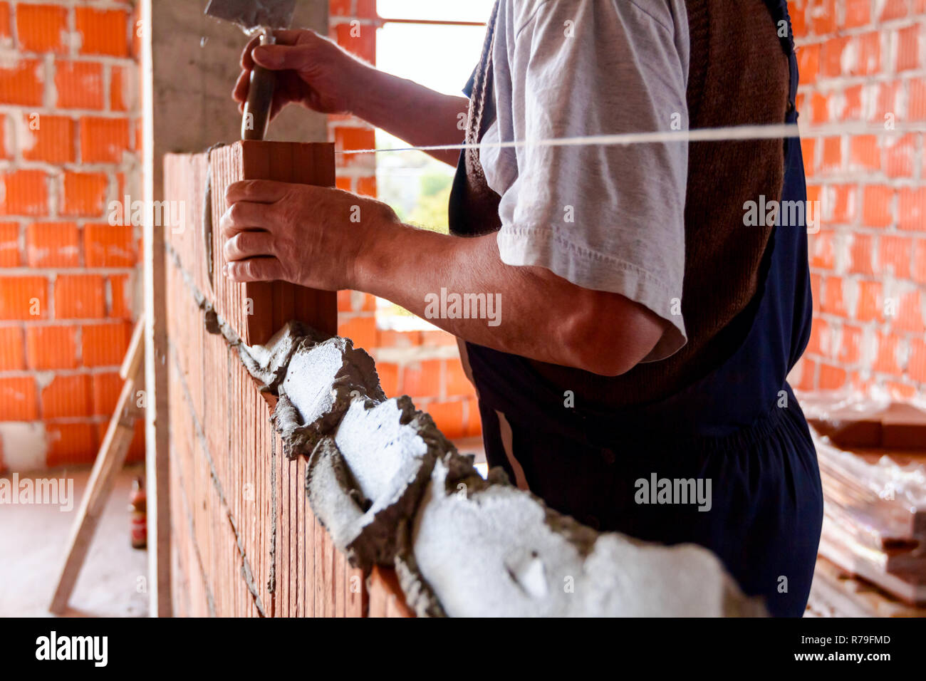 Mason, bricklayer worker is using red blocks to mount a wall next the string  line to be straight Stock Photo - Alamy