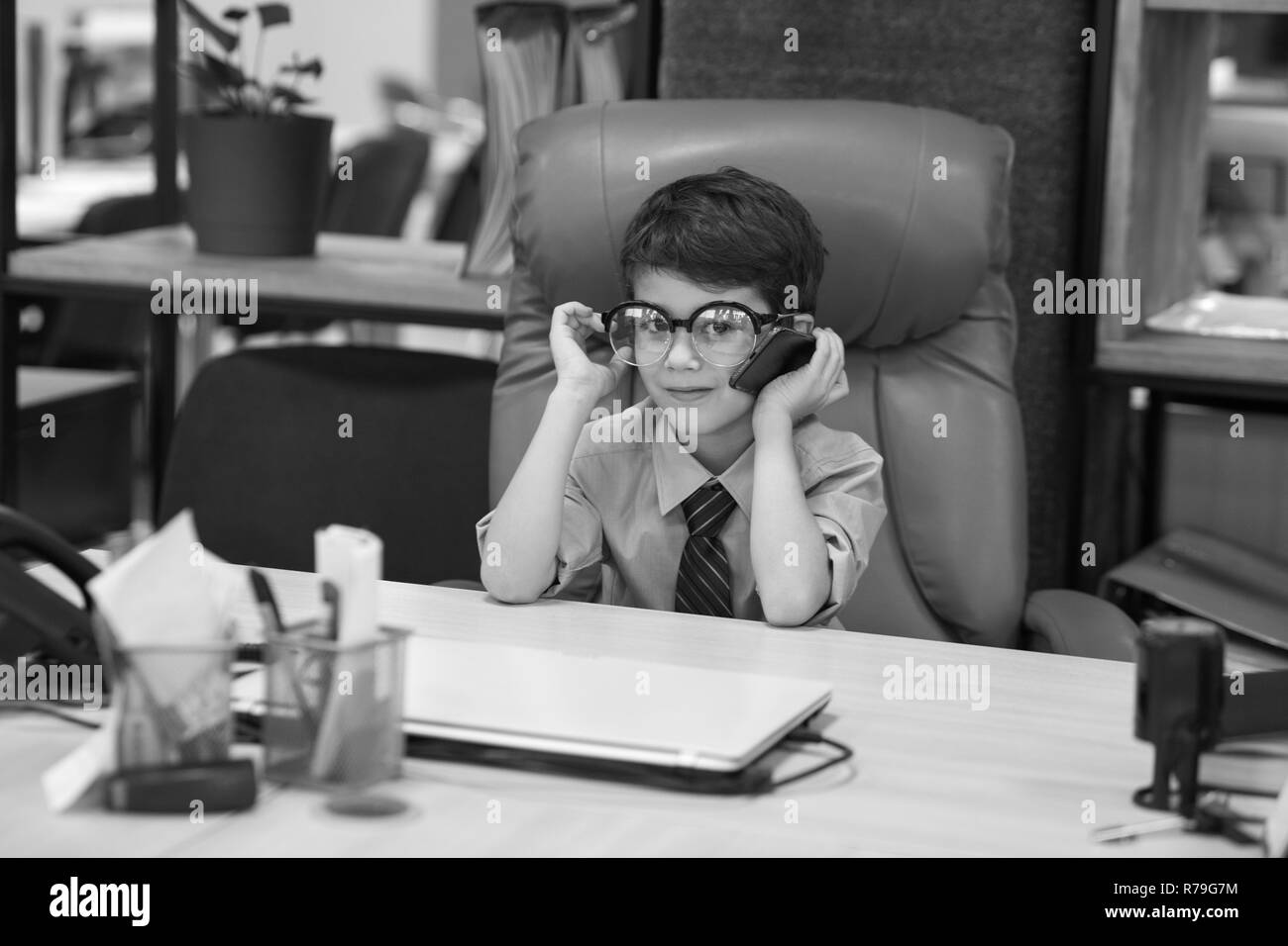 Boy sits in the office in the chair and talking on the phone. Little boss. Stock Photo