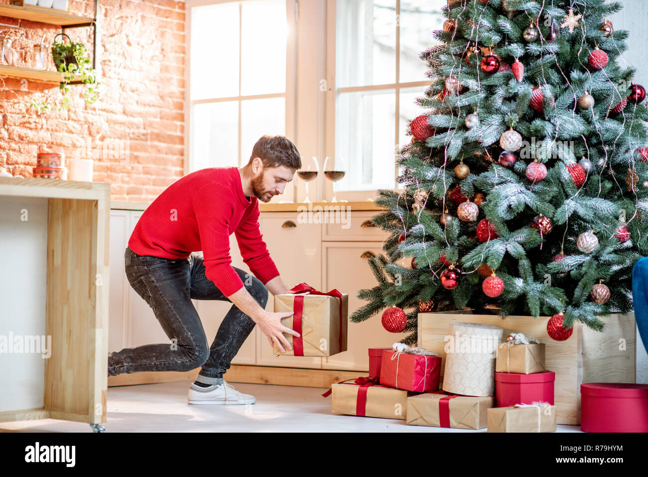 Man putting gifts under the Christmas tree preparing for a New Year  holidays at home Stock Photo - Alamy
