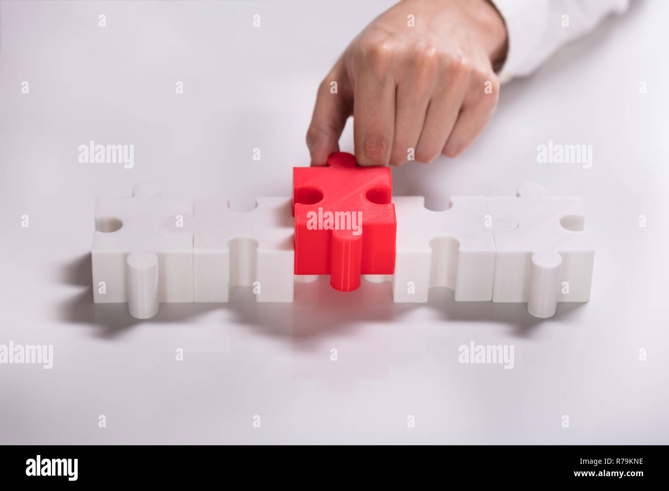 Person Placing Red Piece Between White Jigsaw Puzzles Stock Photo