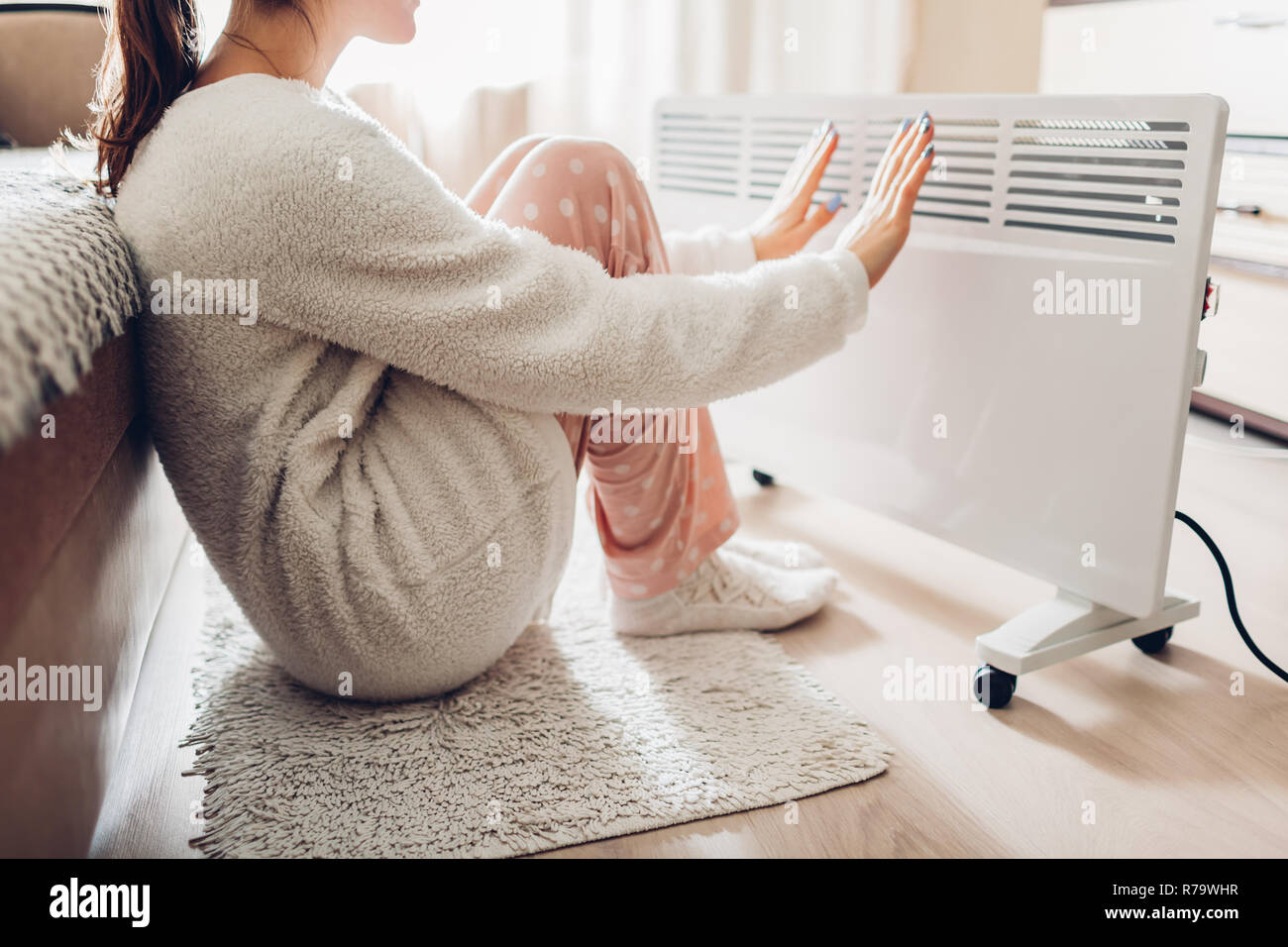 Using heater at home in winter. Woman warming her hands sitting by