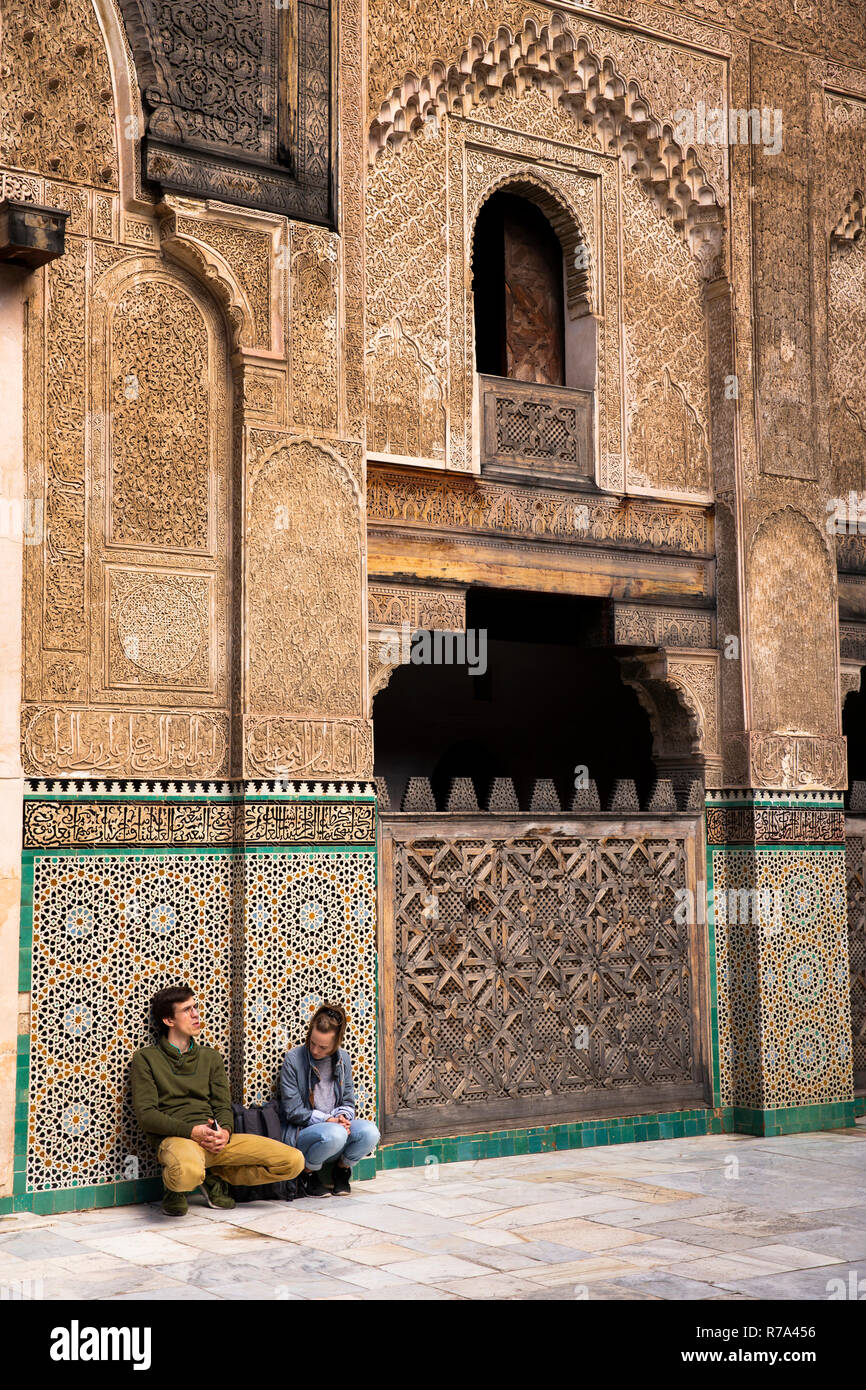 Morocco, Fes, Fes el Bali, Medina, Talaa Seghira, Medersa Bou Inania, young tourists sat in courtyard surrounded by highly decorated walls Stock Photo