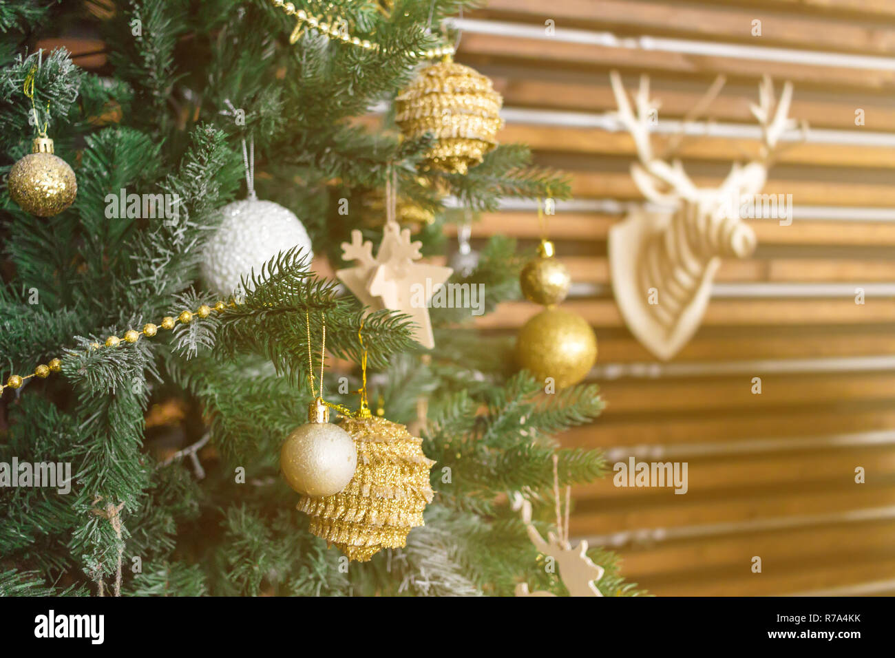 Christmas tree with golden balls, star, beads, other decorations. Deer head model on the wall as background. New Year Theme concept. Sun shining orang Stock Photo