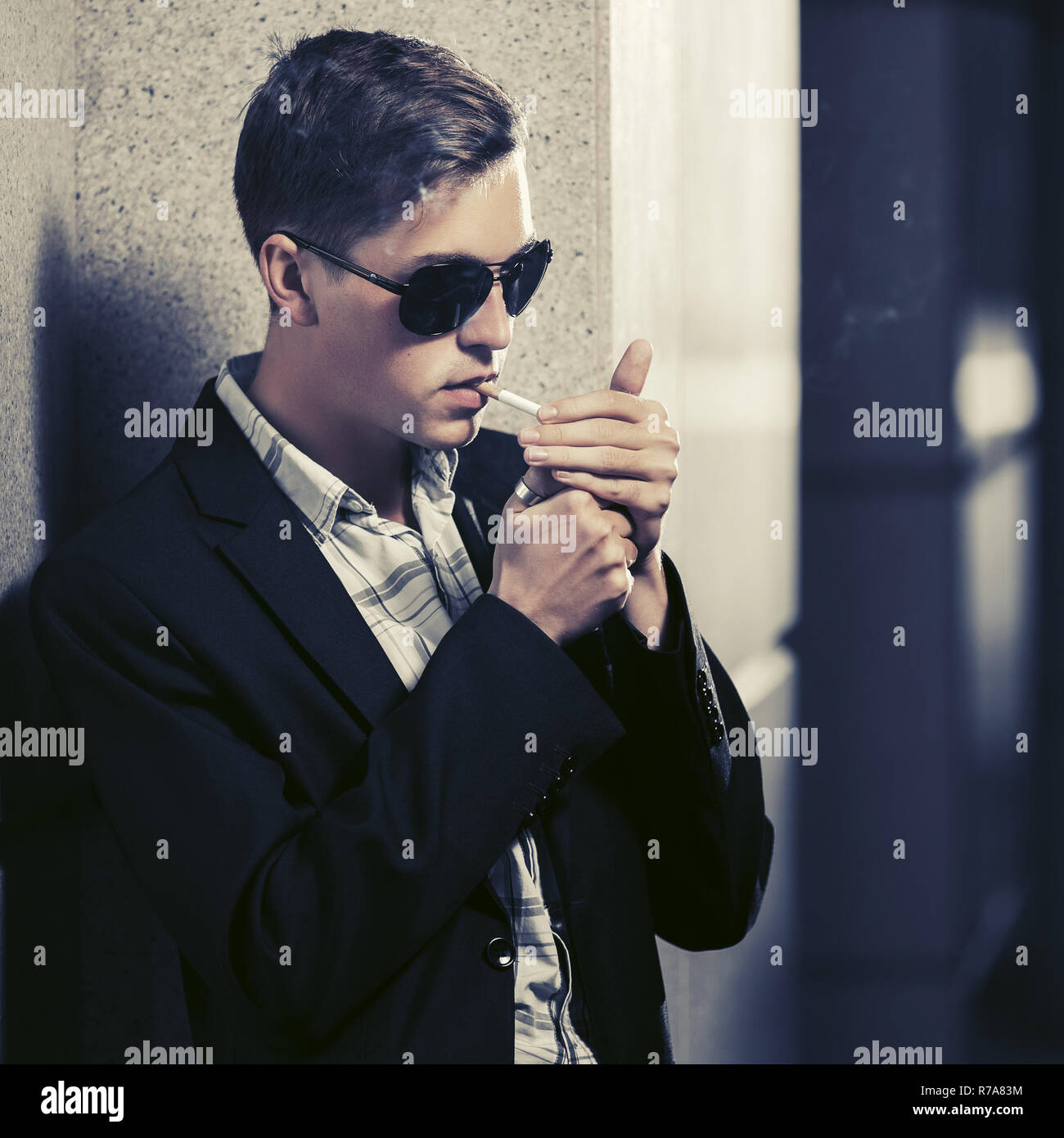 Young handsome man in sunglasses smoking a cigarette in city street Stylish fashion male model in black blazer Stock Photo