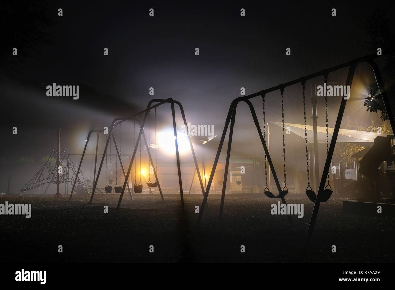 Swing sets backlit by streetlights on a dark foggy morning. Lake Benson