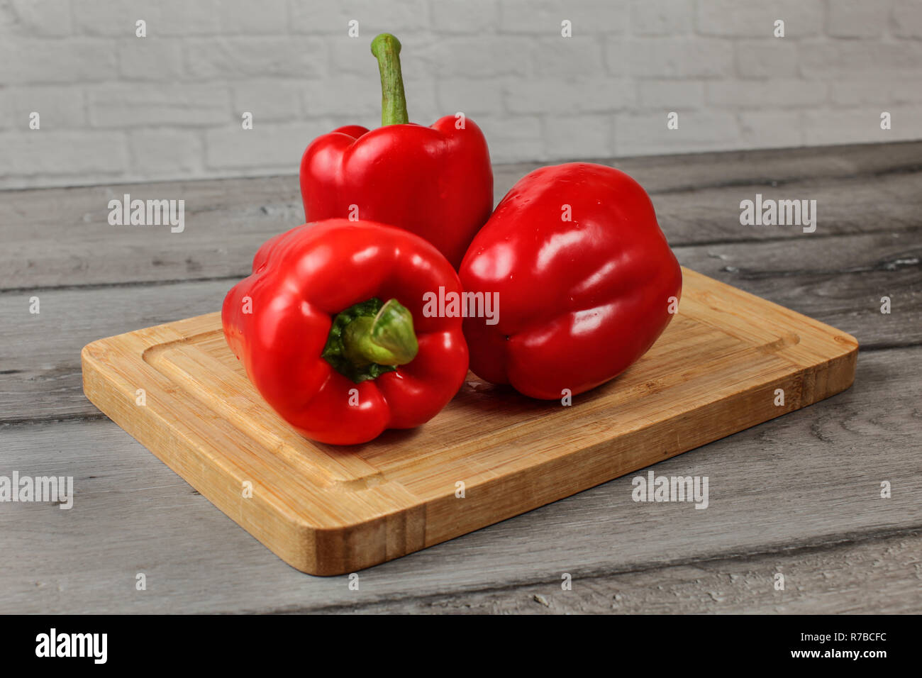 Three whole red bell peppers on chopping board Stock Photo - Alamy