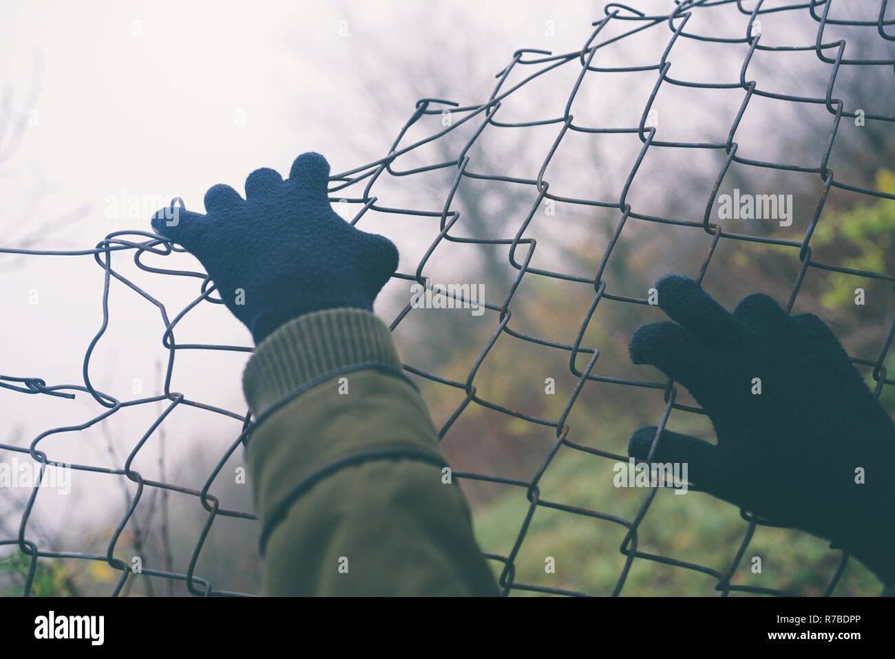 Gloved Hands on Wire Fence on an Overcast Day Closeup Stock Photo