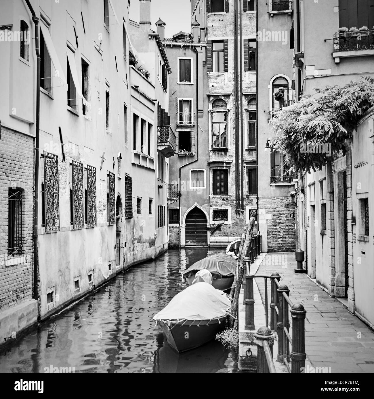Narrow side canal with moored motorboats in Venice, Italy. Black and white image Stock Photo