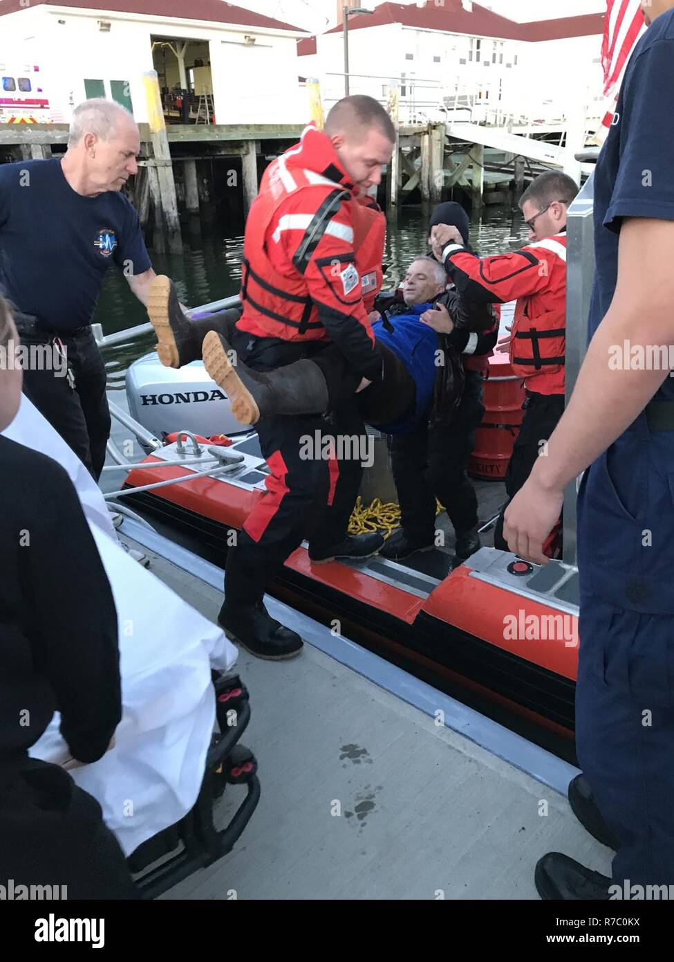 NEW YORK - Coast Guard crewmembers from Station Fire Island help transfer a man they rescued to Emergency Medical Service personnel on May 16, 2017, in Babylon, New York. The man overturned in his kayak and spent over an hour clinging to a mooring buoy before the rescue crew arrived on scene. Stock Photo