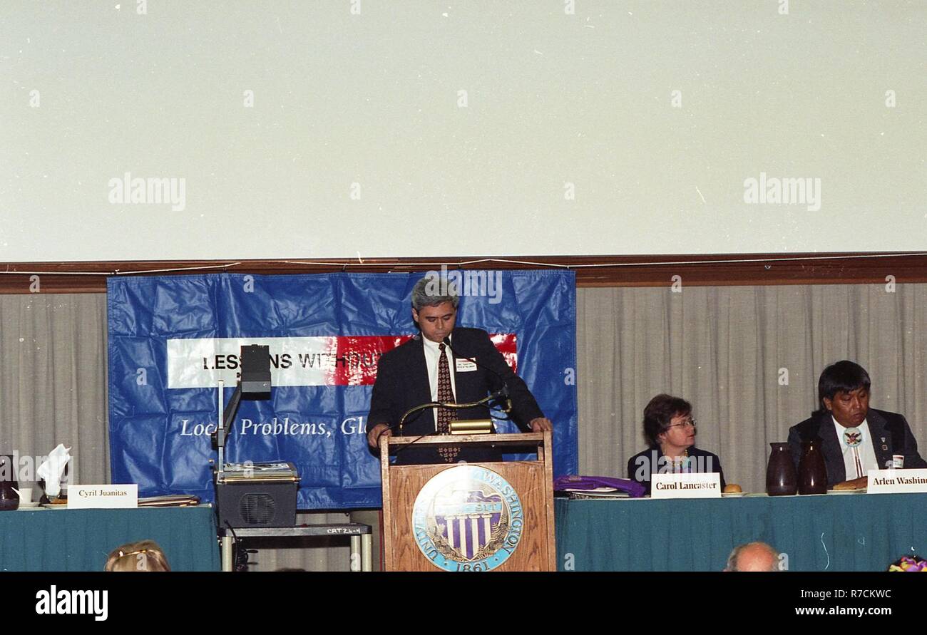 A MAN GIVING A SPEECH AT THE PODIUM WITH TWO OTHER PEOPLE ON STAGE ...