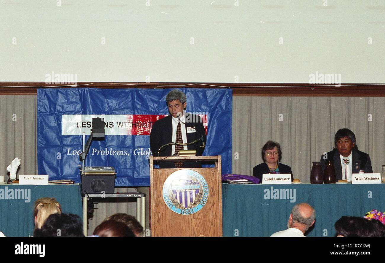A MAN GIVING A SPEECH AT THE PODIUM WITH TWO OTHER PEOPLE ON STAGE ...