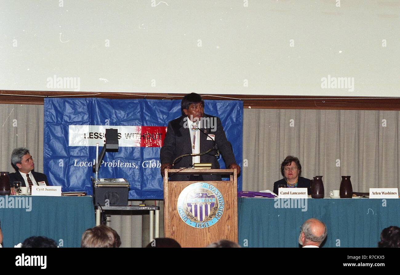 A MAN GIVING A SPEECH AT THE PODIUM WITH TWO OTHER PEOPLE ON STAGE ...