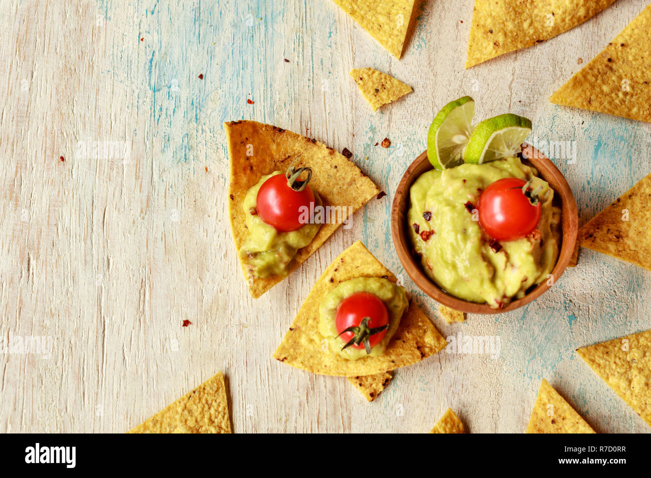 Corn chips nachos and guacamole in a wooden bowl decorated with cherry tomatoes and lime slices on a wooden white washed table. Eith space. Stock Photo