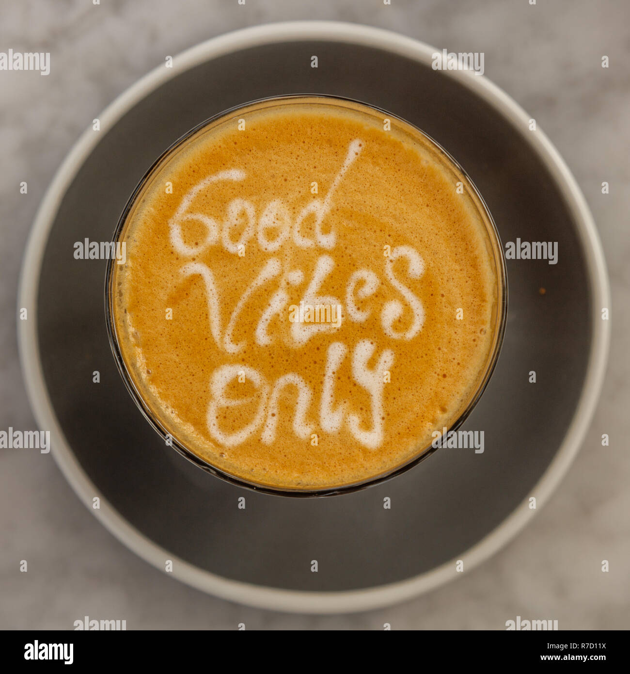 Cup of coffee latte on a while table, with Good Vibes Only latte art and a chocolate cookie on the side. Square image. Stock Photo