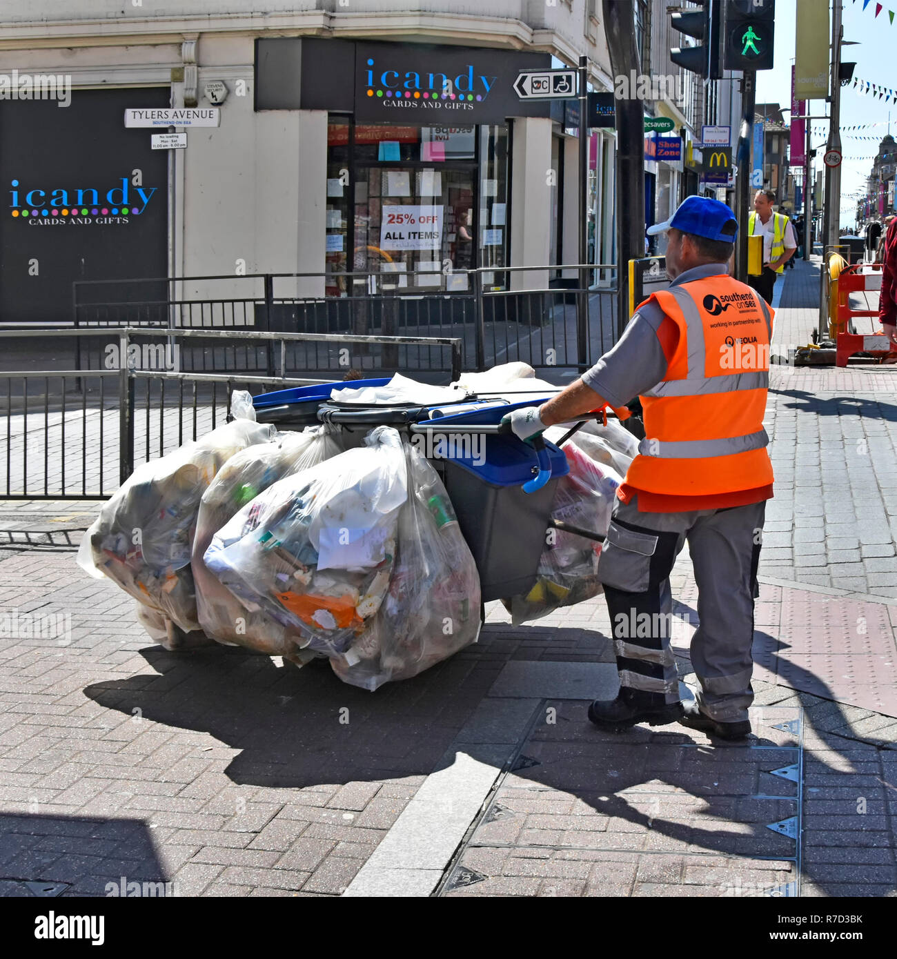 Bins sacks & bags full of litter rubbish on garbage hand cart in shopping street pushed by council worker collected from seaside resort pavement bins Stock Photo