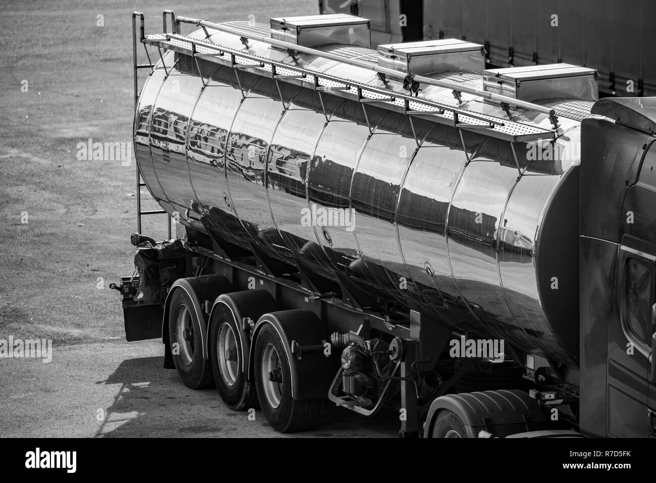 The rear-side part of shiny tin fuel truck, black and white side high-angle view reflecting containers in an open area Stock Photo