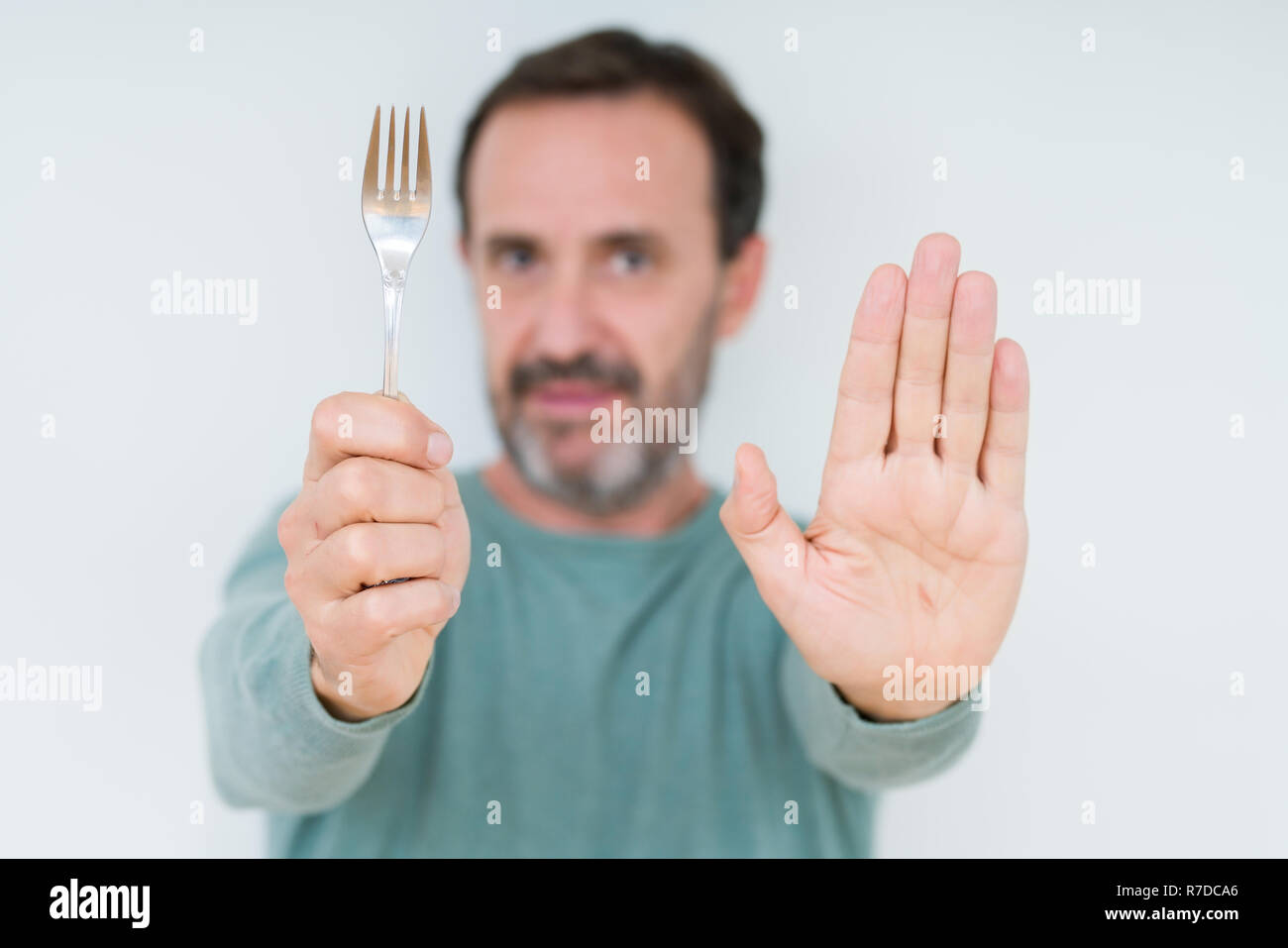 Senior man holding silver fork over isolated background with open hand