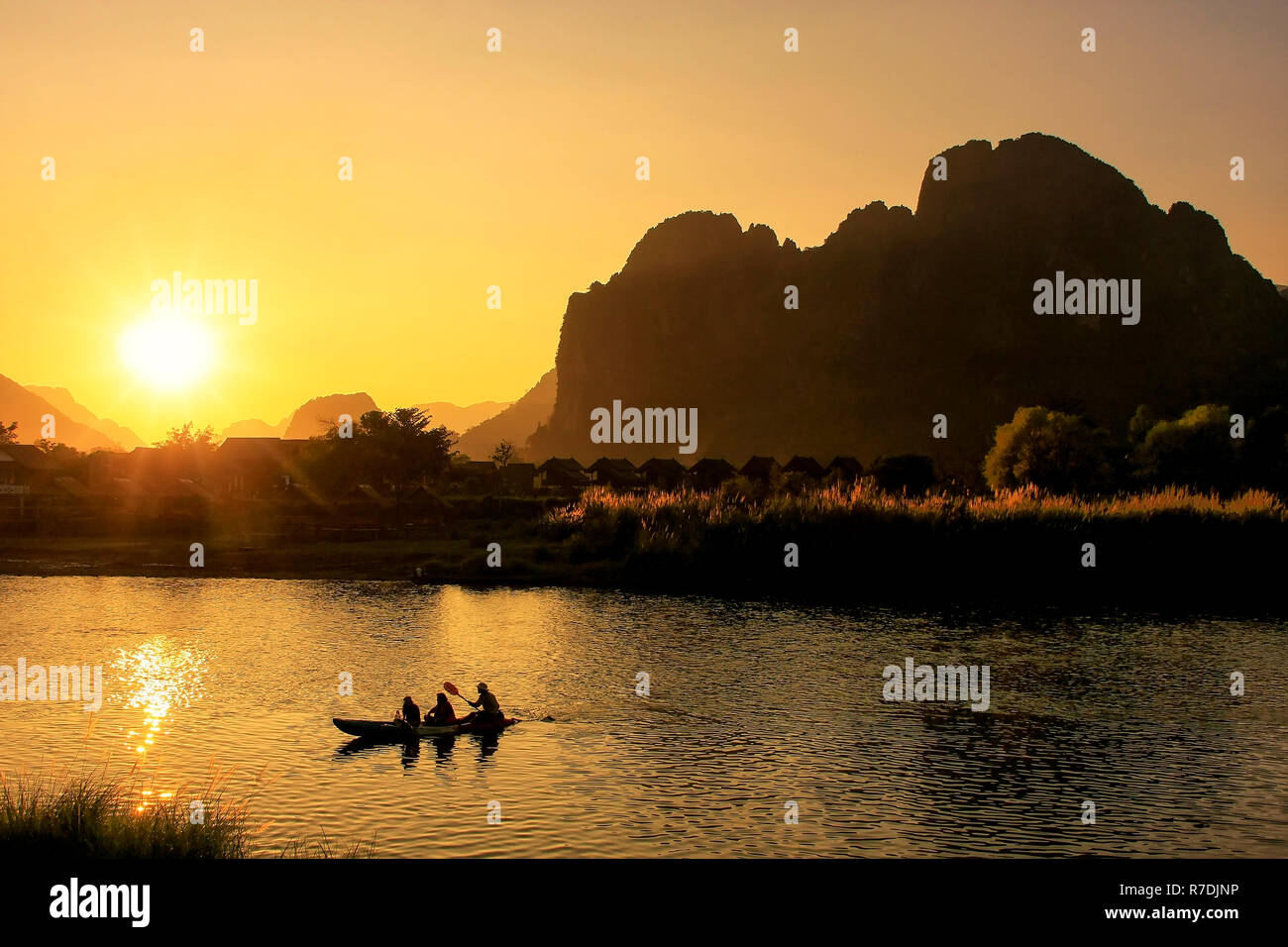 Nam Song River at sunset with silhouetted rock formations and kayakers in Vang Vieng, Laos. Vang Vieng is a popular destination for adventure tourism  Stock Photo