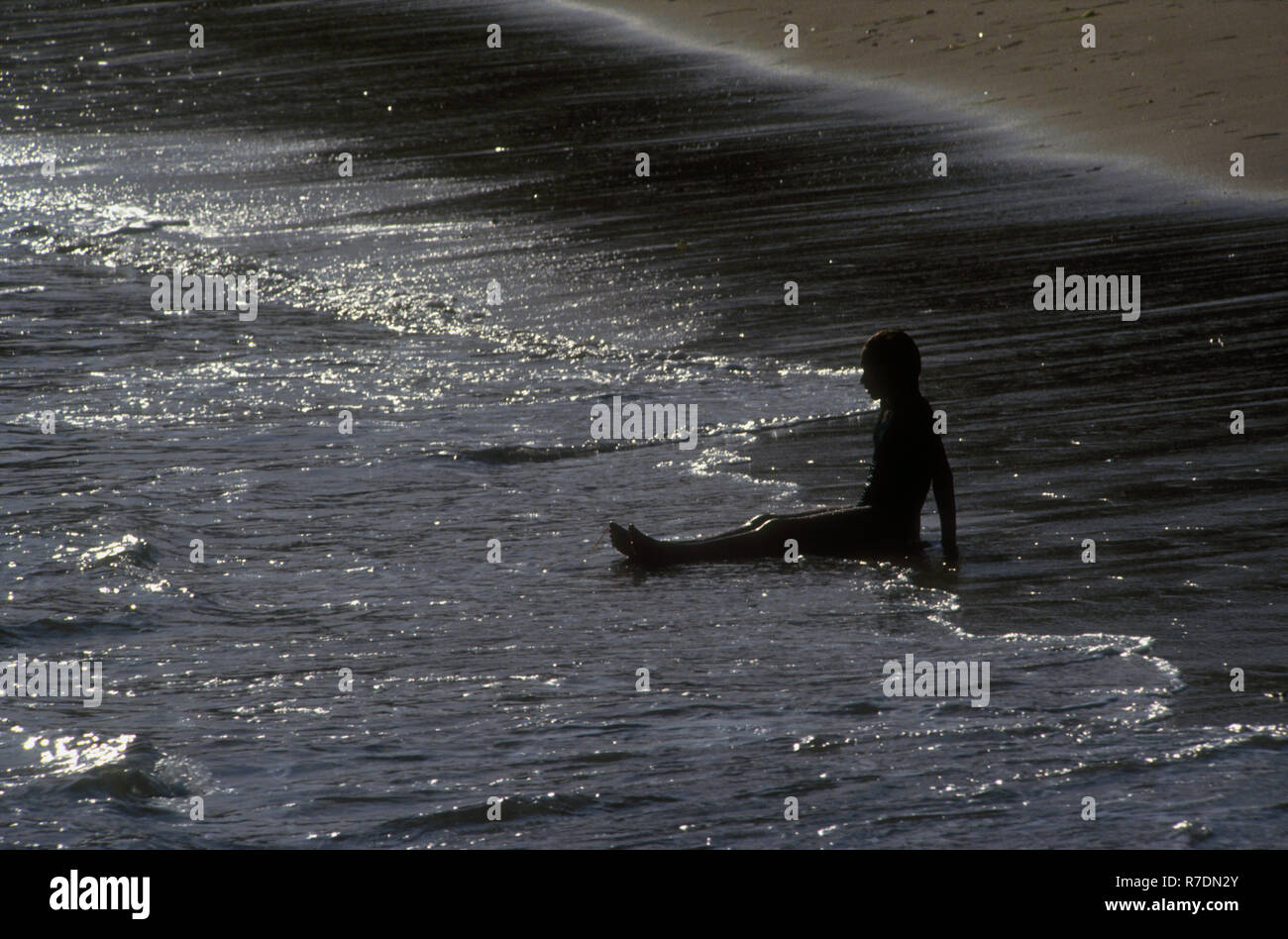 TEENAGE GIRL SITTING ALONE IN THE SURF, SHOAL BAY, NEW SOUTH WALES, AUSTRALIA Stock Photo