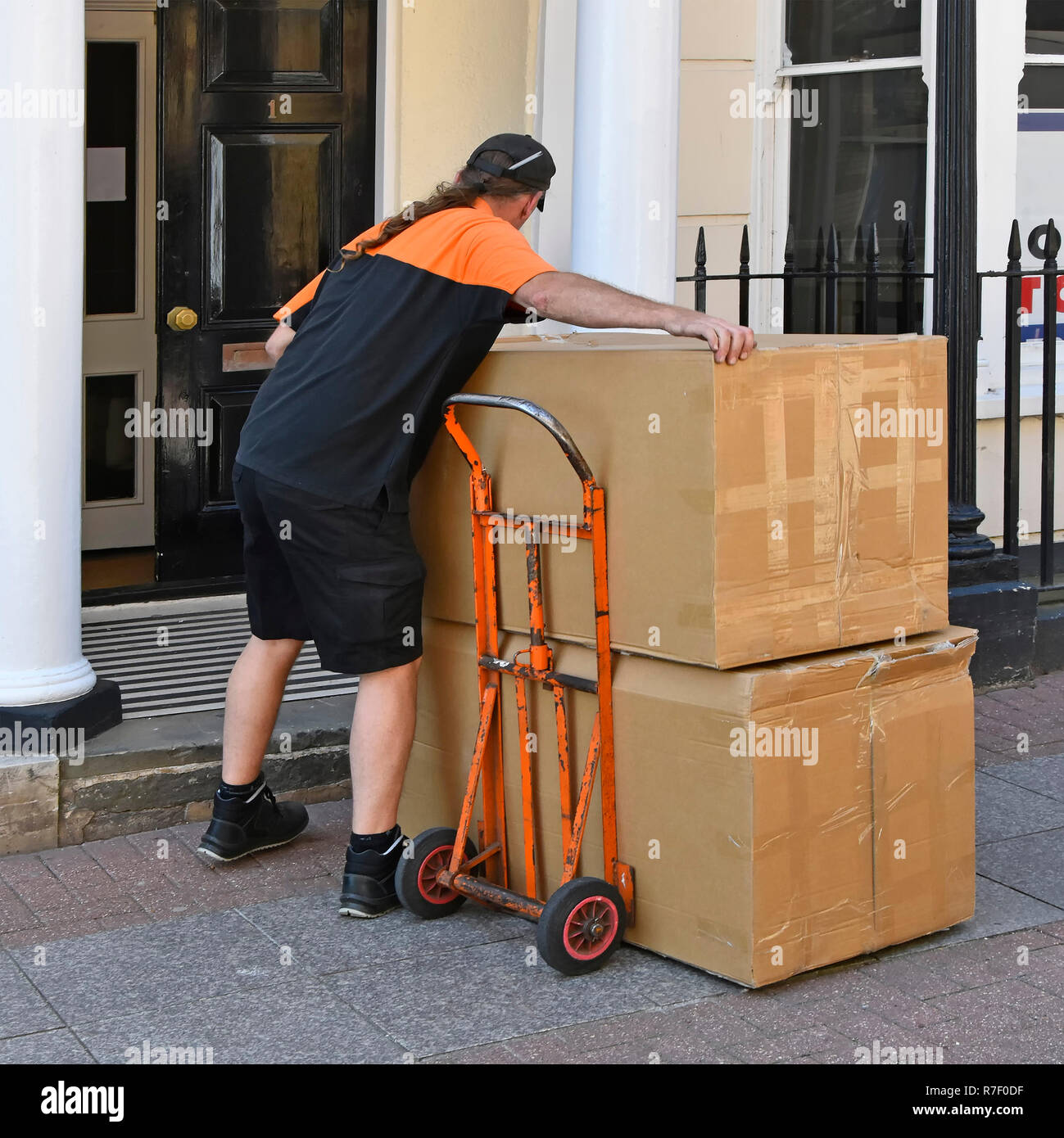 Man working as a TNT parcel delivery driver lifting cardboard box from trolley to deliver at narrow entrance door  Southend on Sea Essex England UK Stock Photo