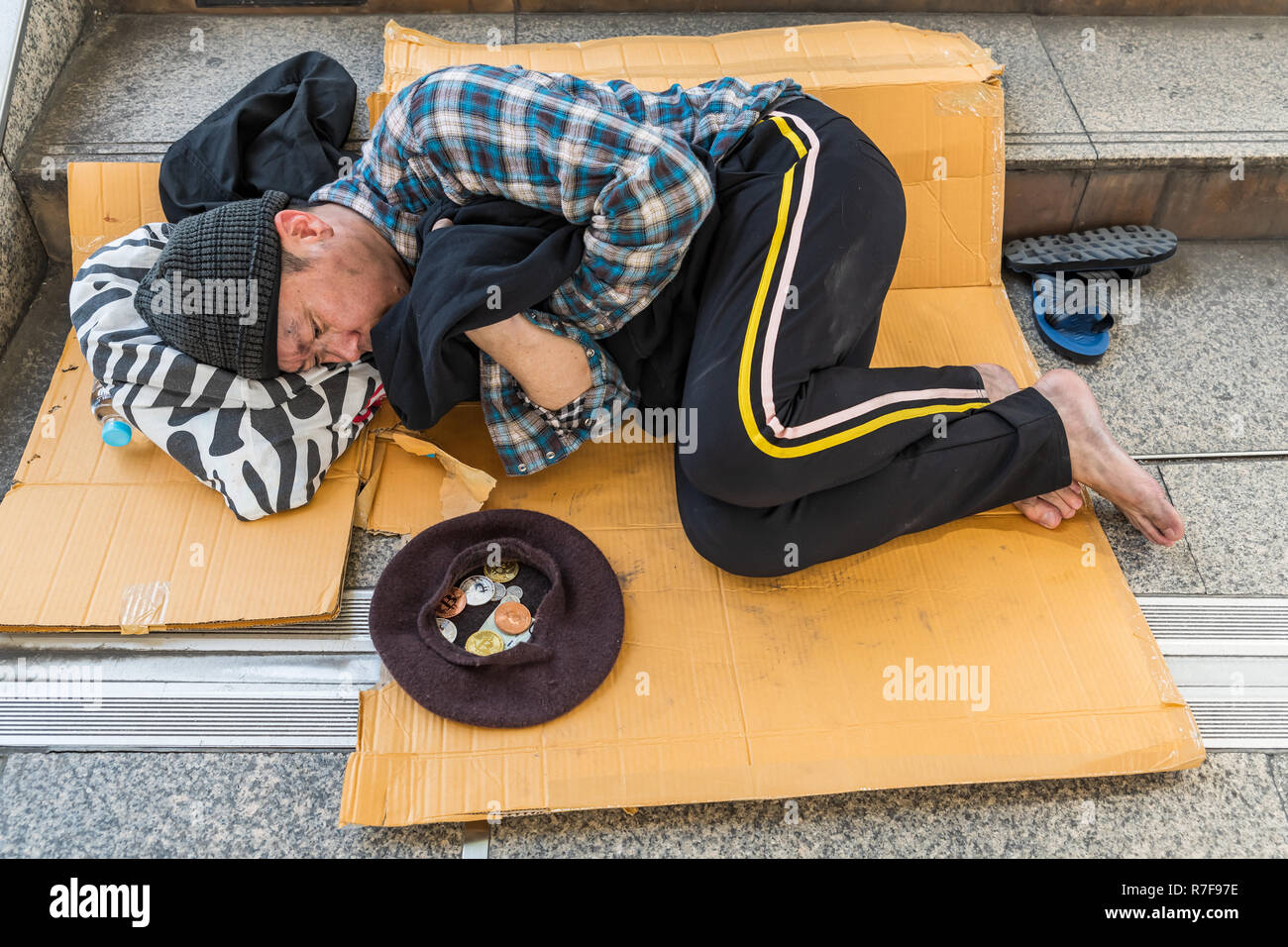 A male homeless beggar looking at the cap with some bitcoin coins inside - devaluation of bitcoin concept Stock Photo