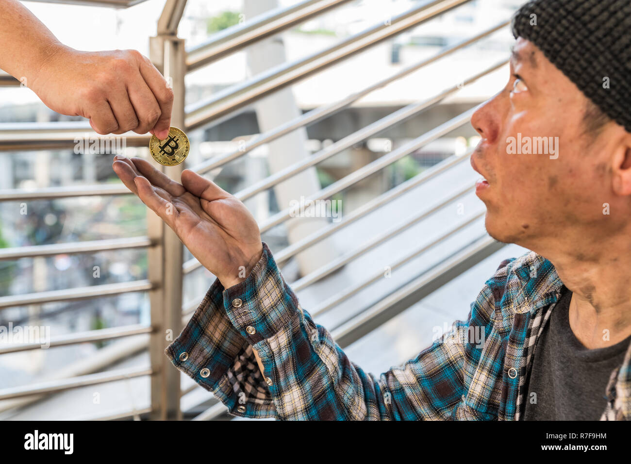 A male homeless beggar receiving a gold bitcoin coin with surprising face - devaluation of bitcoin concept Stock Photo
