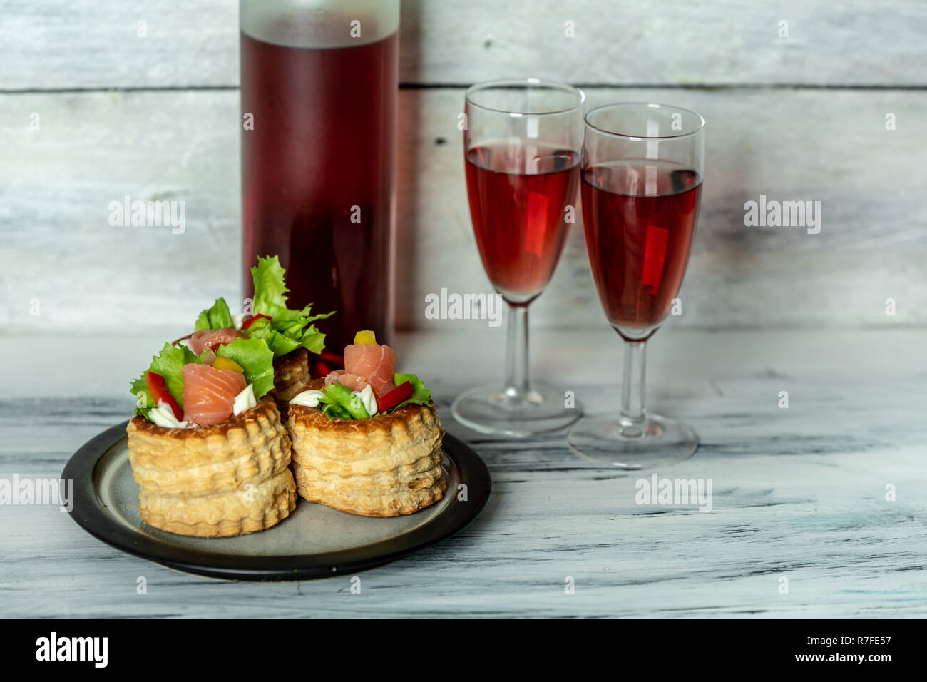 French cuisine, crunchy patties with lettuce and smoked salmon on a bright, rustic background, next to a glass of red wine Stock Photo