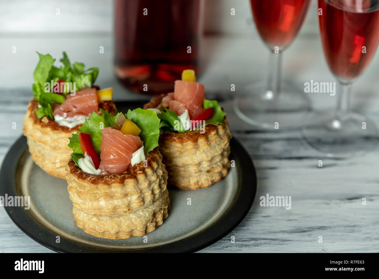 French cuisine, crunchy patties with lettuce and smoked salmon on a bright, rustic background, next to a glass of red wine Stock Photo