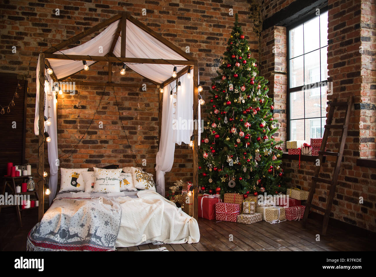 bed with canopy valance baldachin decorated with decorative pillows with a pattern and lamps . Christmas tree with gifts loft style brick wall. new ye Stock Photo