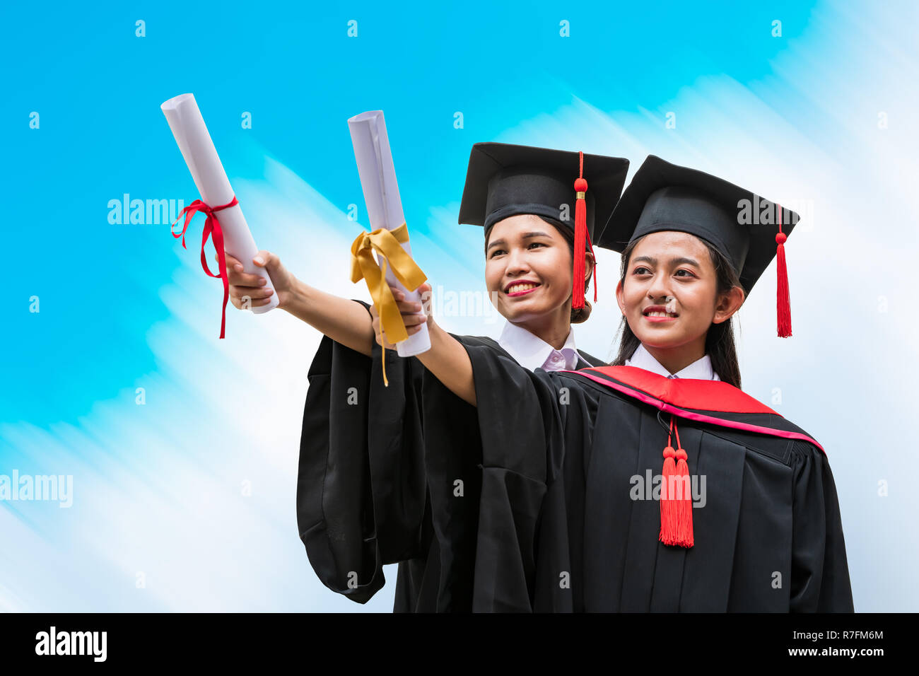 Two female Asian students in graduation gown holding the diplomas Stock Pho...