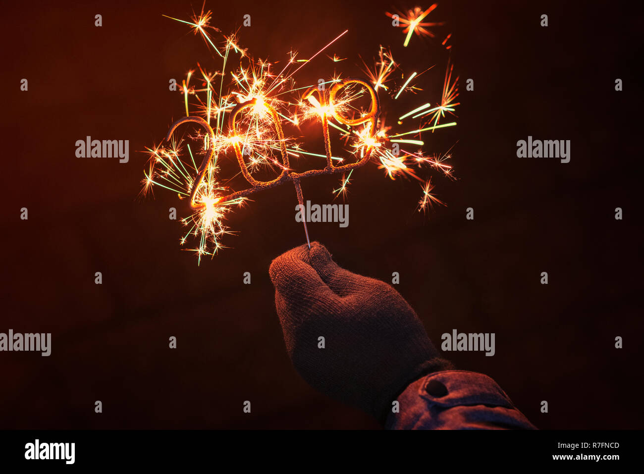 Human hand with glove holding an igniting 2019 Shaped Sparkler, outdoors at night Stock Photo