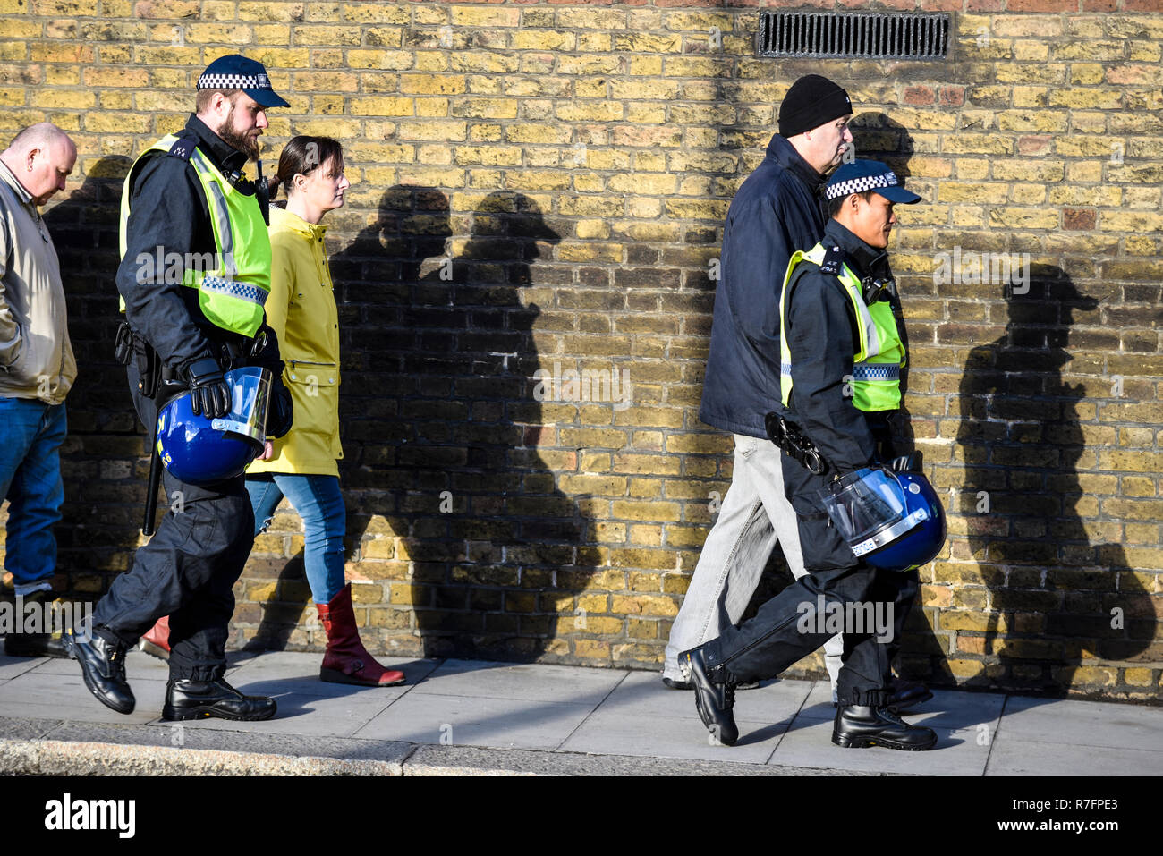 Brexit Betrayal March in London days before the planned Parliament vote. Police escort walking with shadows on wall in bright sunlight. People Stock Photo