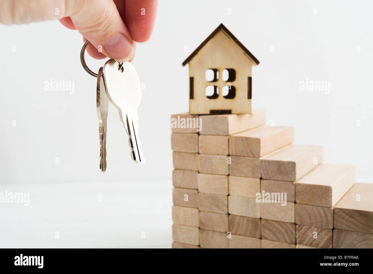 Woman hand hold two keys from house with toy wooden house on stairs with copy space Stock Photo